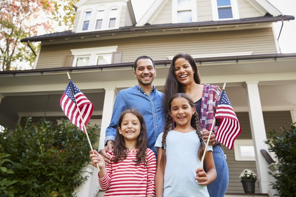 A family on the front porch of their home waving American flags.