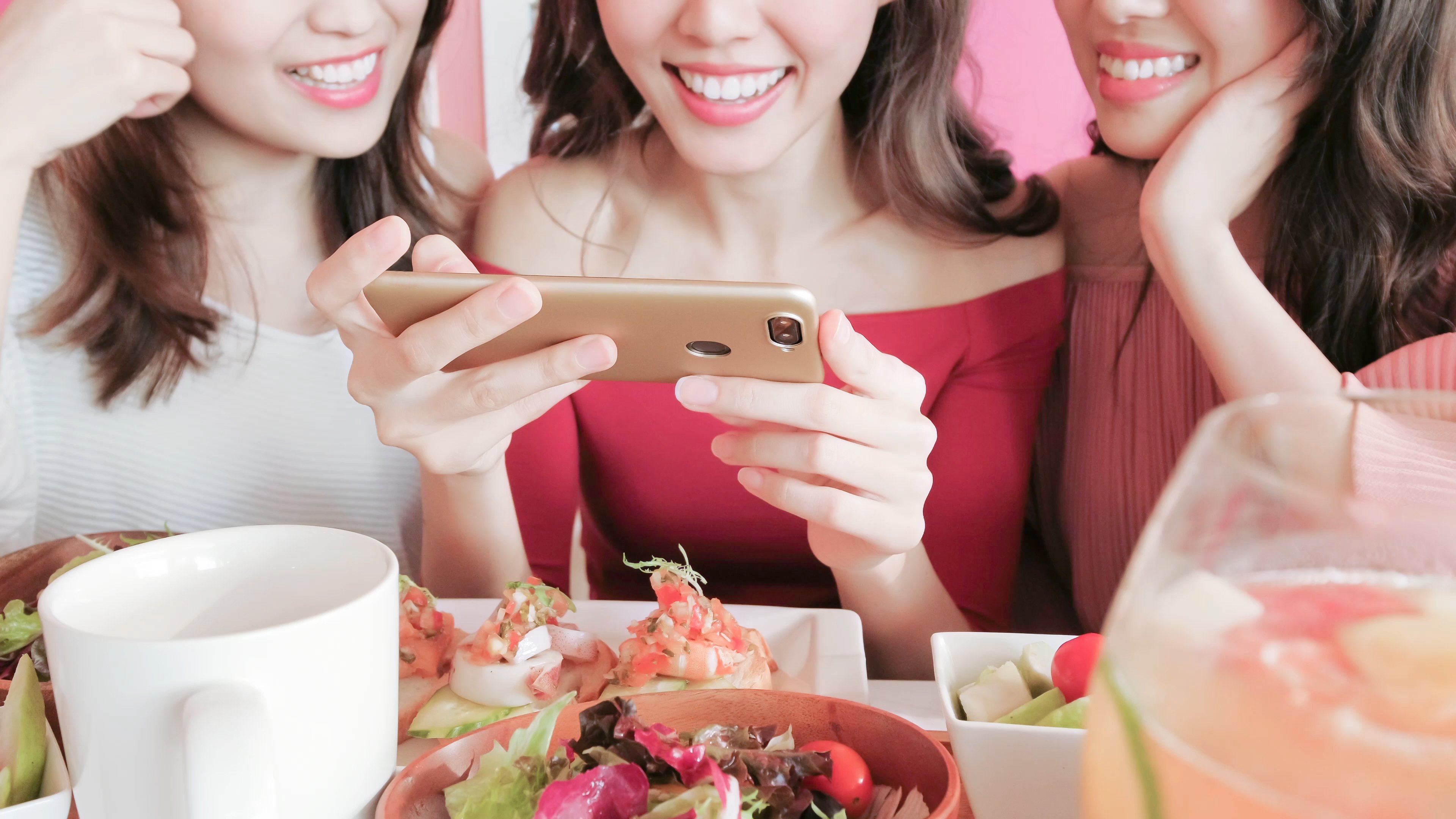 Three women take photos of their food with a smartphone.