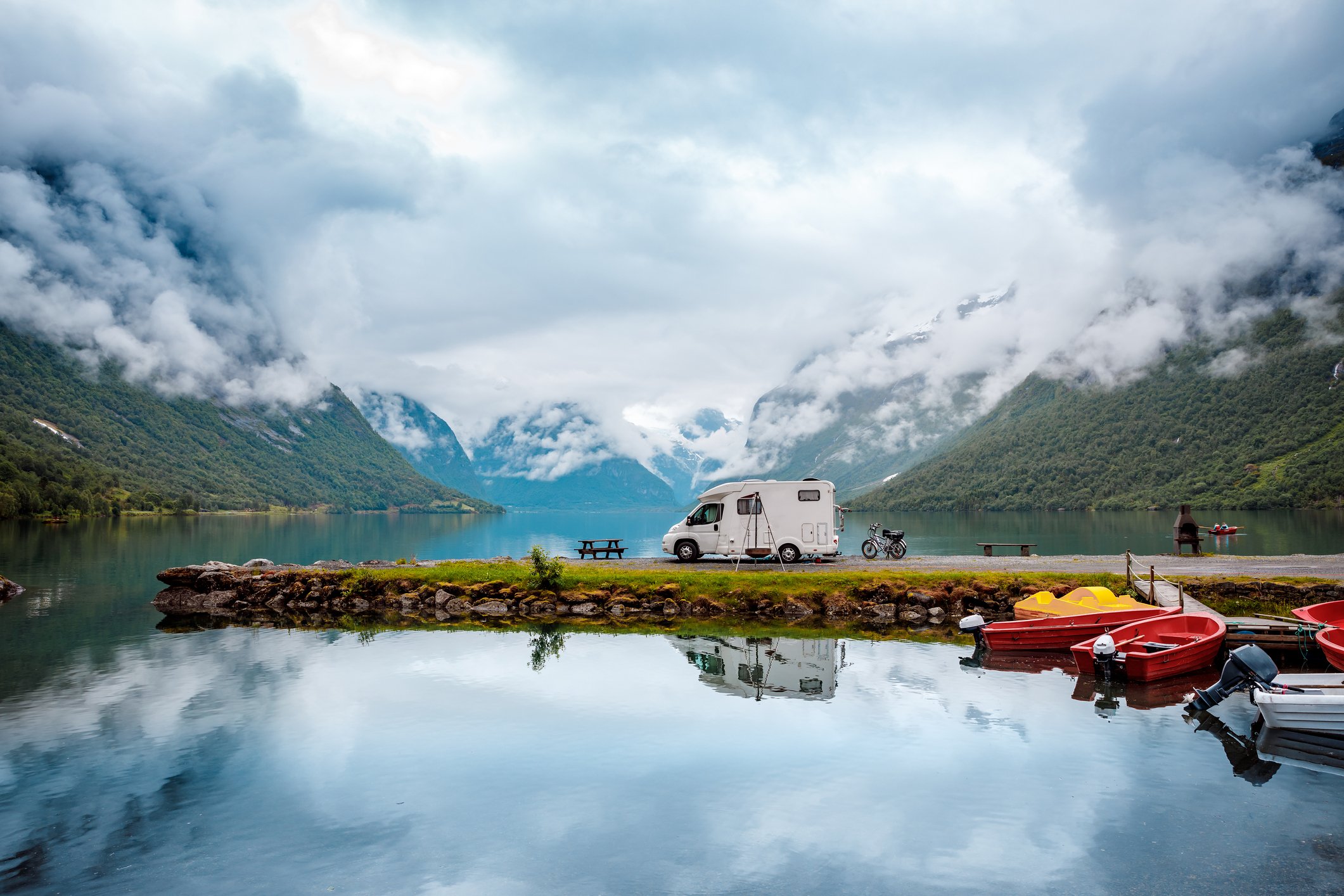 RV parked on a spit of land jutting into a lake, surrounded by boats