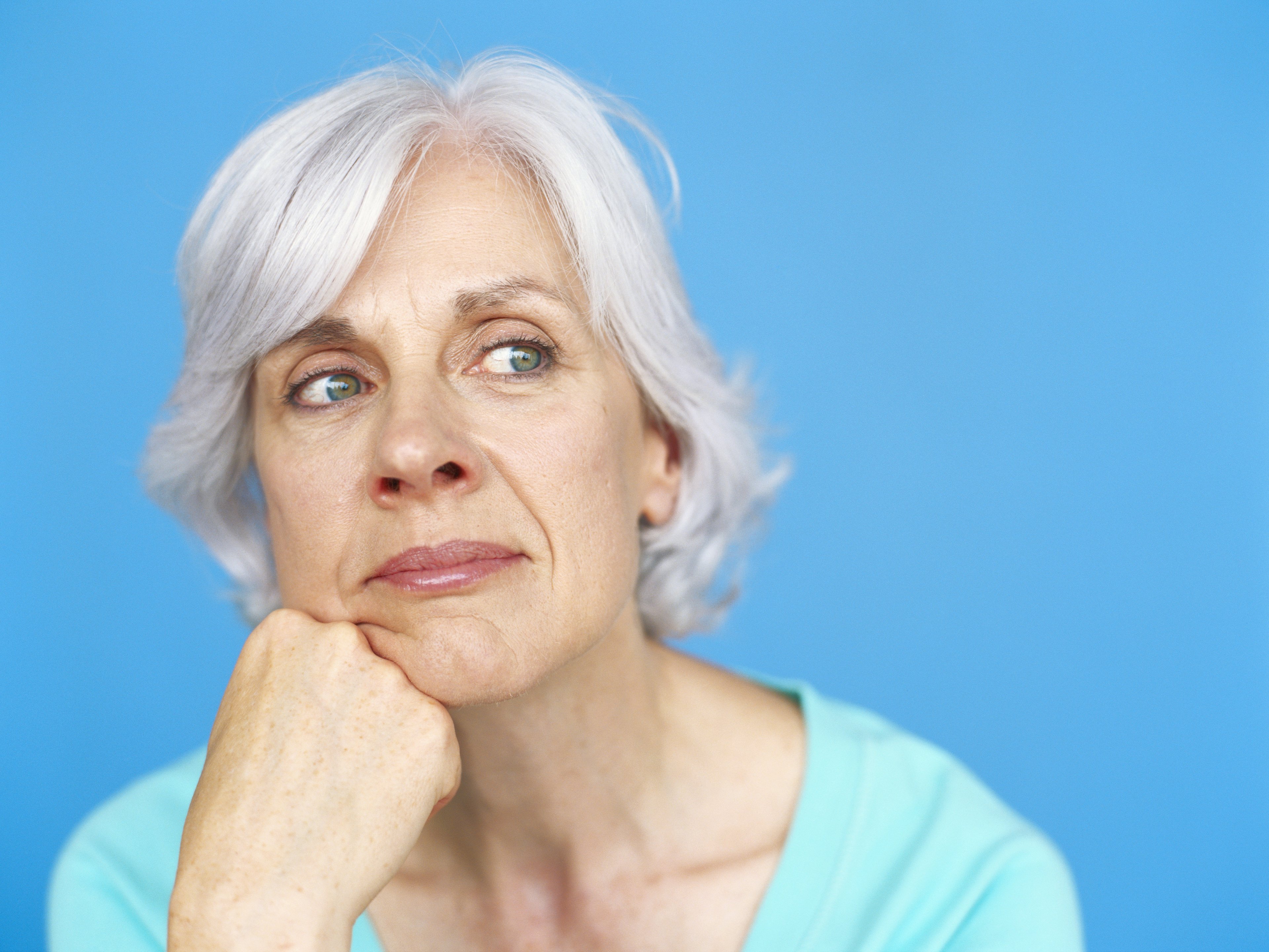 Mature woman thinking with chin on fist against blue background