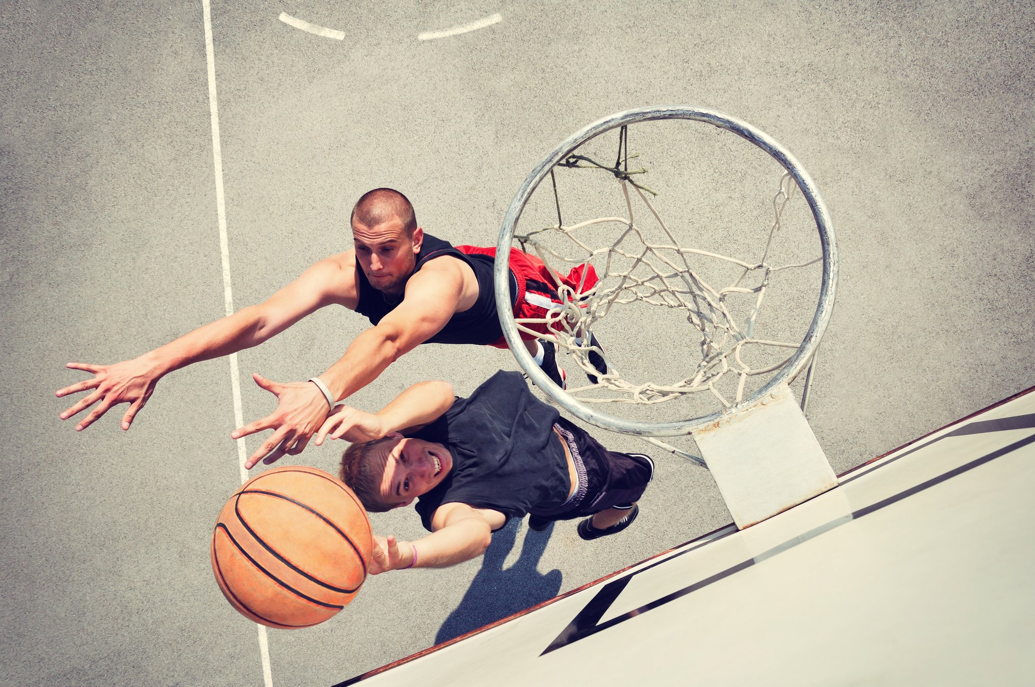 Two players battle over a basketball under the hoop.