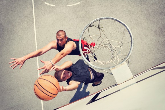 Two players battle over a basketball under the hoop.