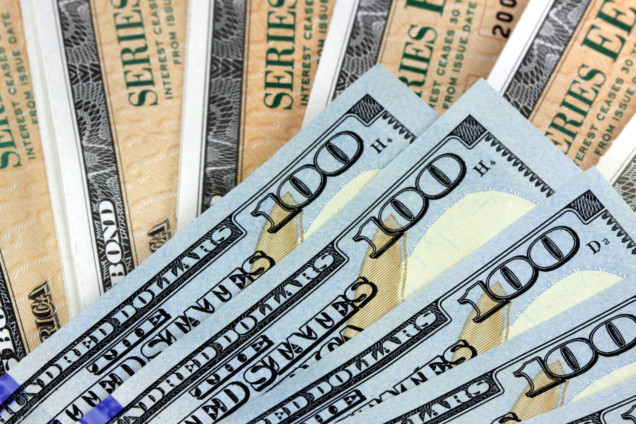 A fanned pile of hundred dollar bills lying atop a fanned stack of Treasury bonds.
