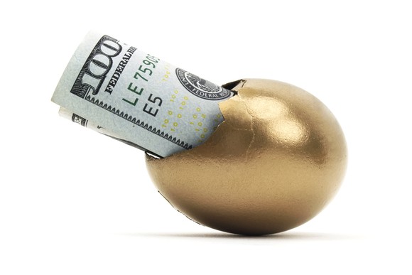 A golden egg with a hundred dollar bill sticking out of a crack in it.