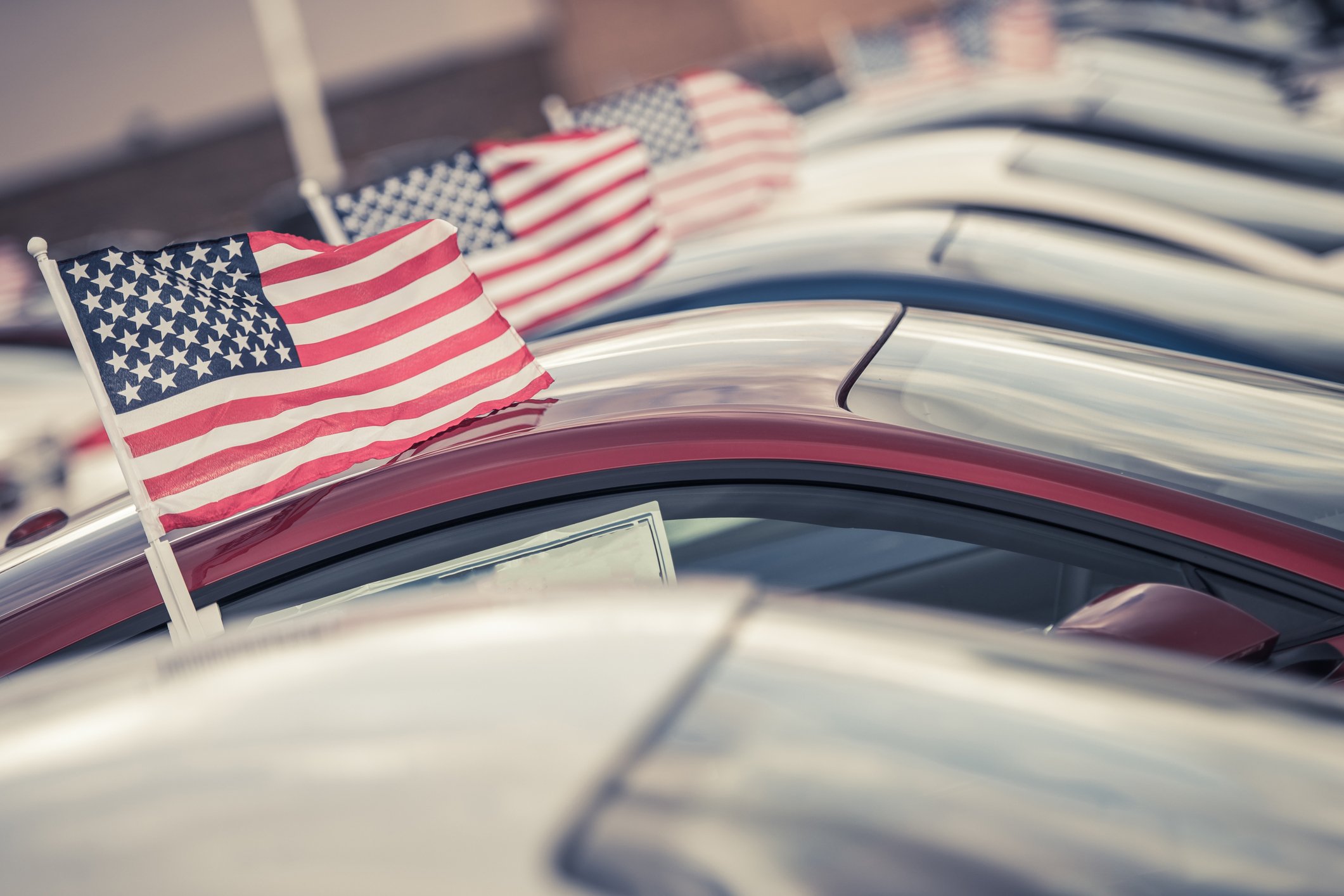 Row of cars at a dealership with American flags on the windows.