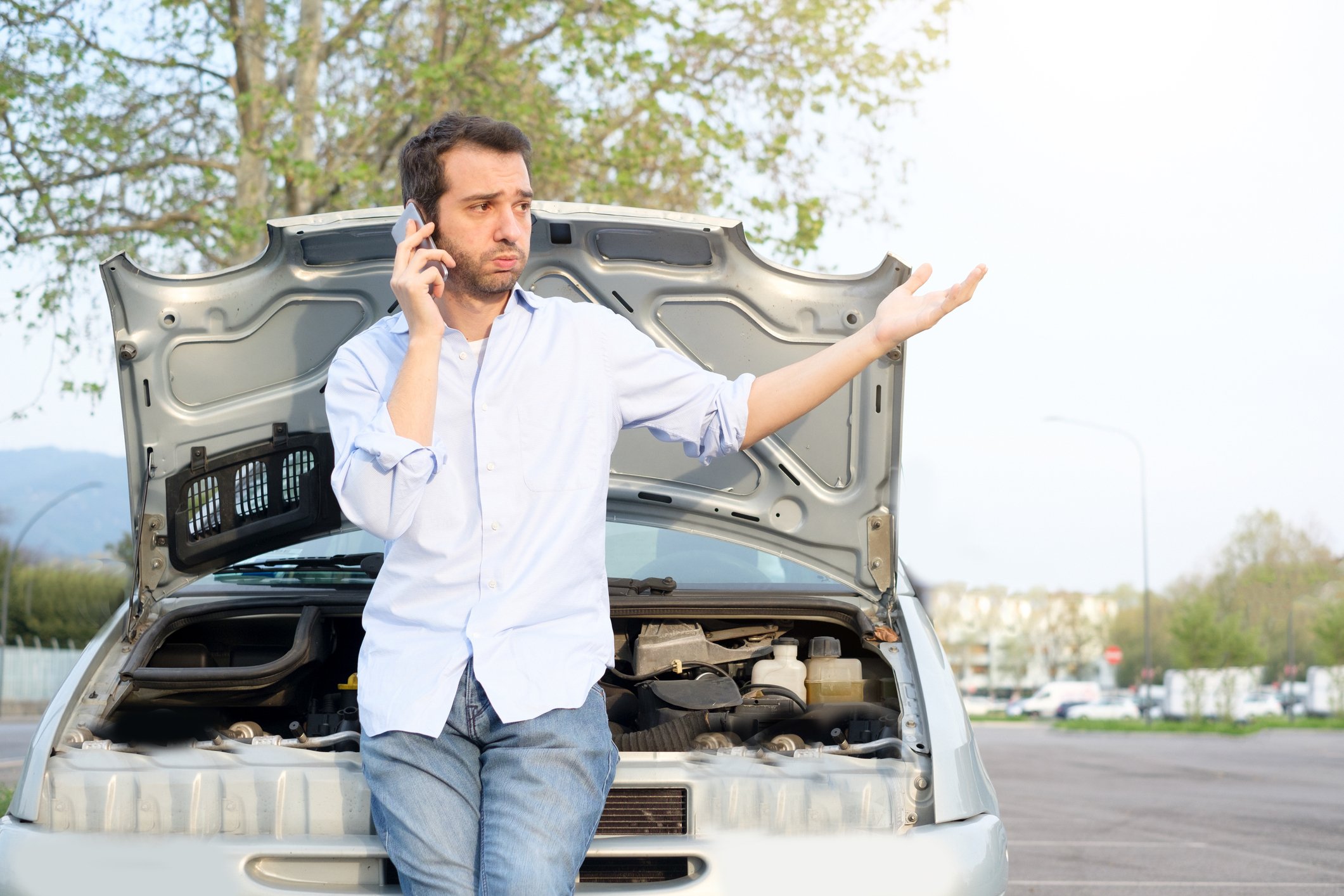 Man on the phone in front of a car with its hood up