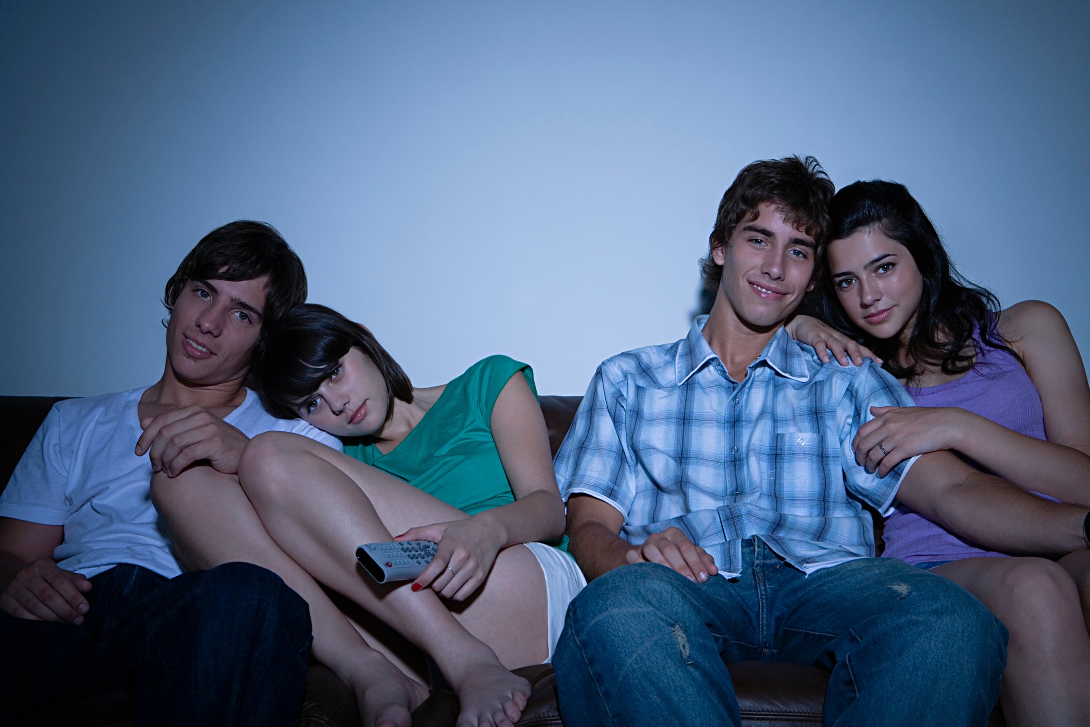 Two couples cuddling on the couch watching TV in a darkened room.