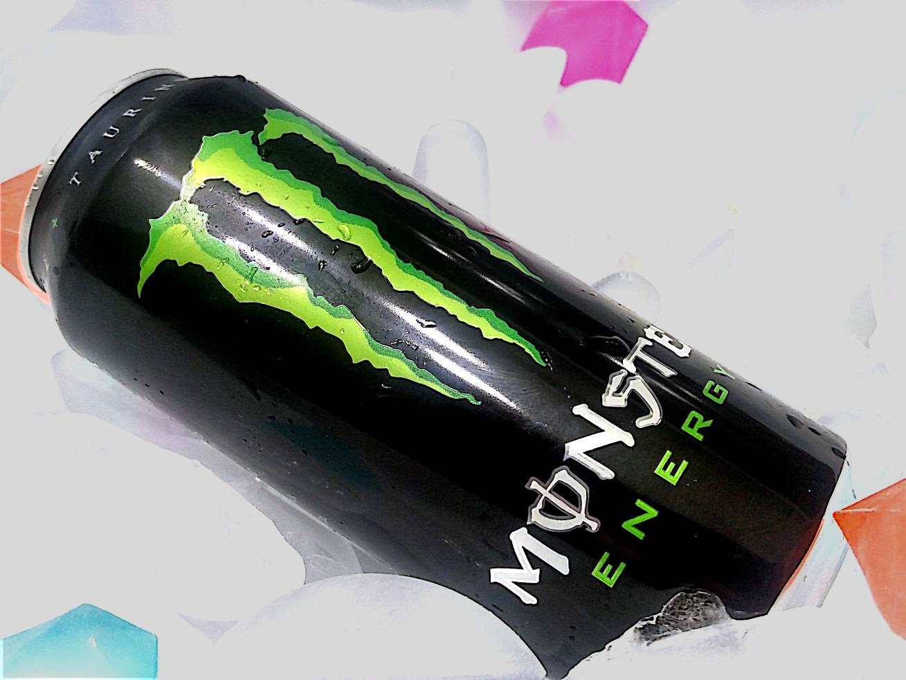 A can of Monster Energy resting on a bed of ice cubes and colorful plastic gems.