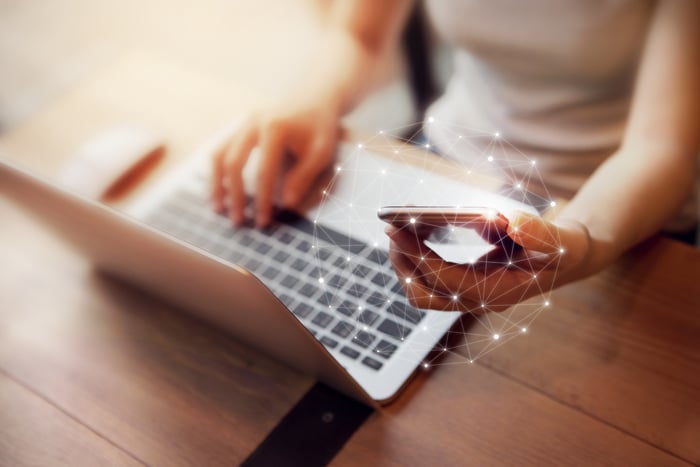 A person using a laptop and holding a mobile phone with a digital web projected around it.