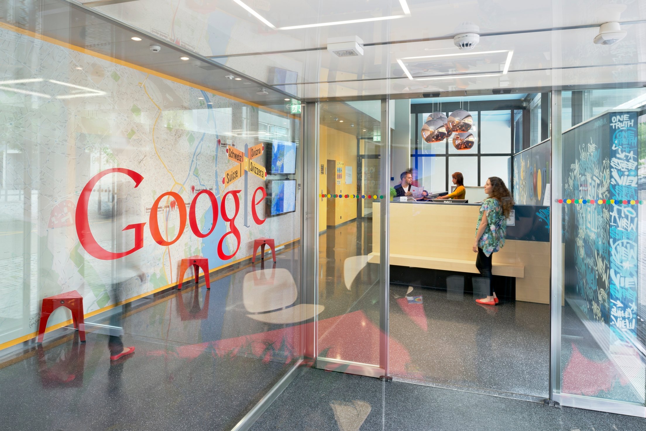A reception desk with several people and Google on a glass entry wall at the company's Zurich HQ entrance.