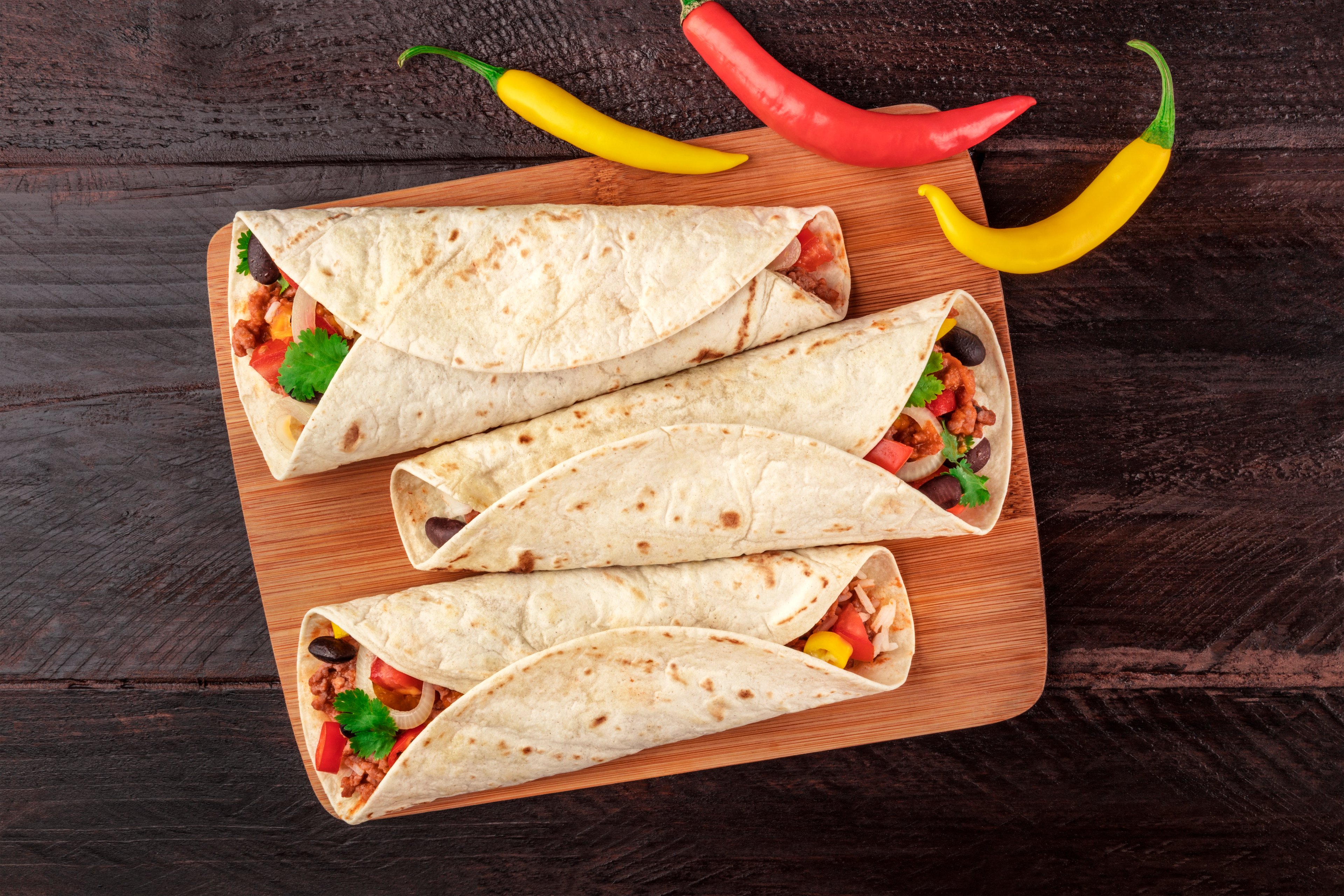 3 burritos on a plate with peppers on the side