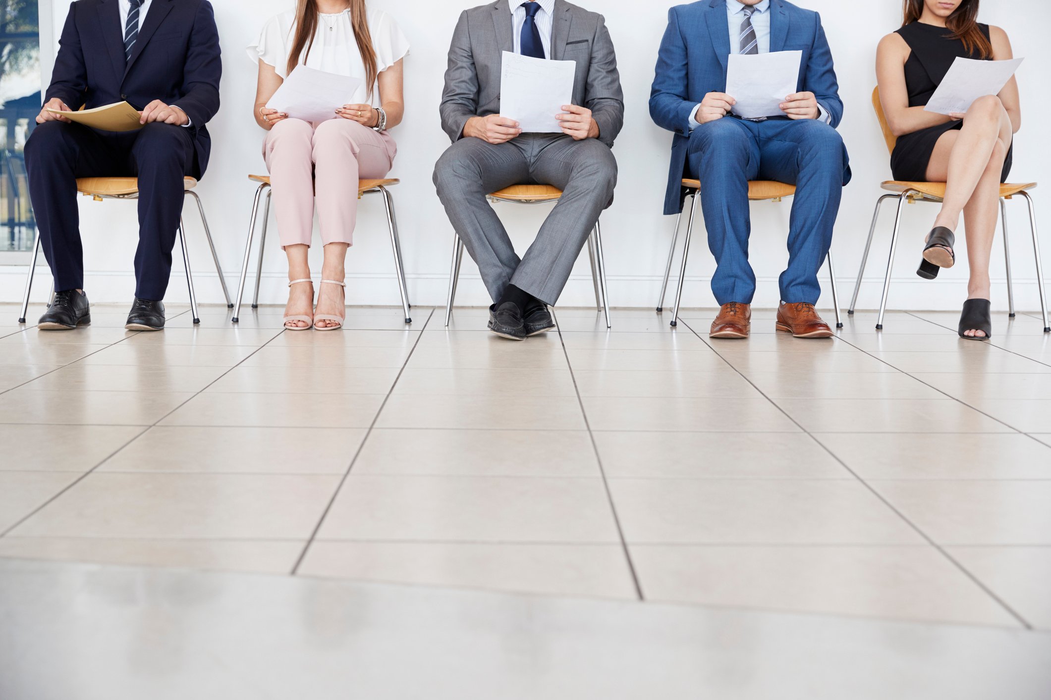 Multiple people sit in a waiting room holding papers.