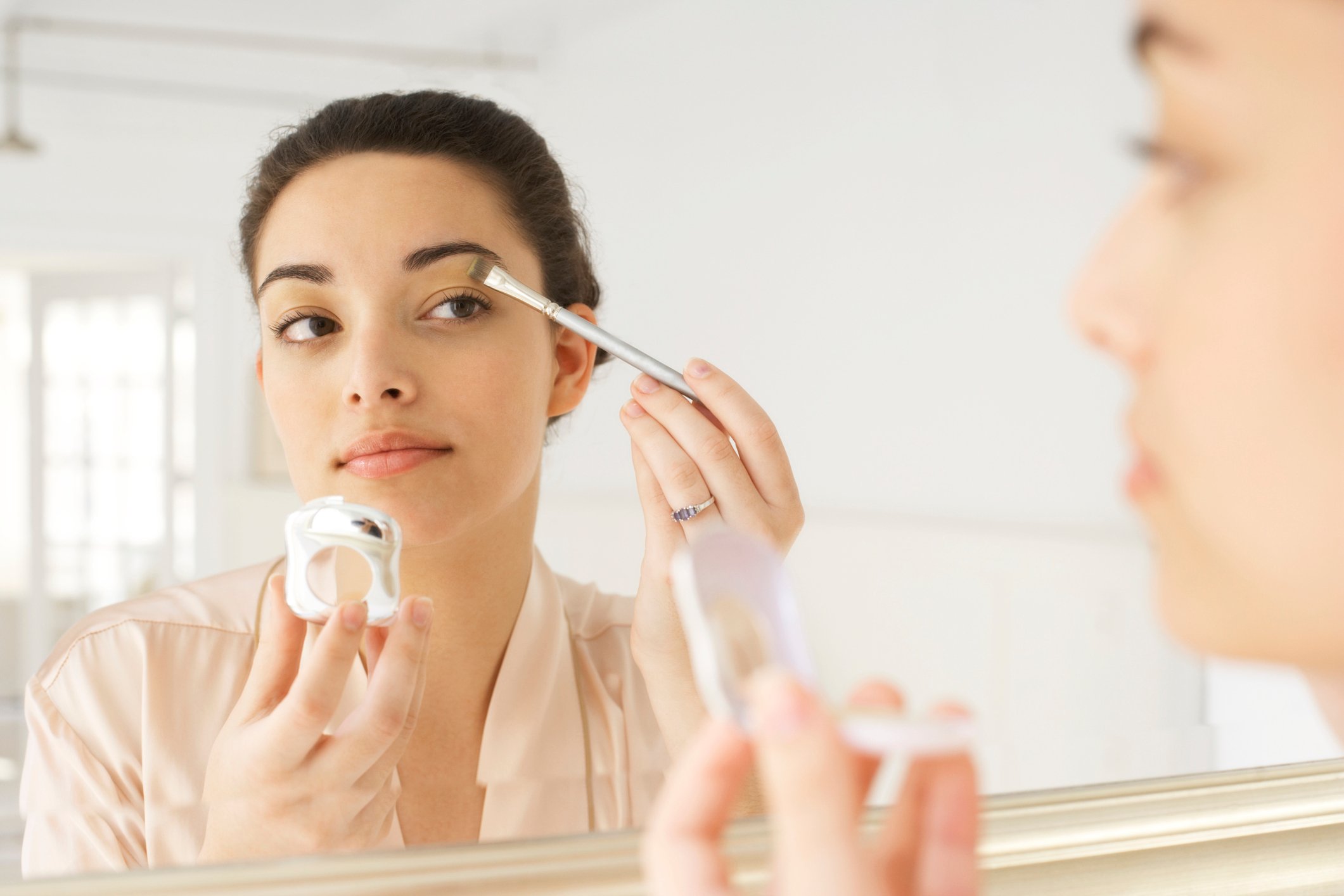A woman applying makeup in the mirror.