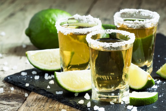 Three shot glasses of tequila with salt and lime