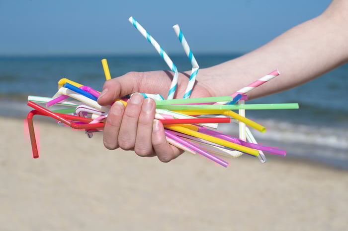 Hand holding plastic straws at beach