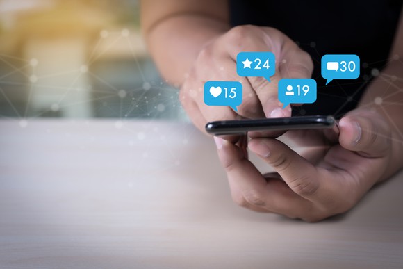 Young man using smart phone with social media icons superimposed above the phone