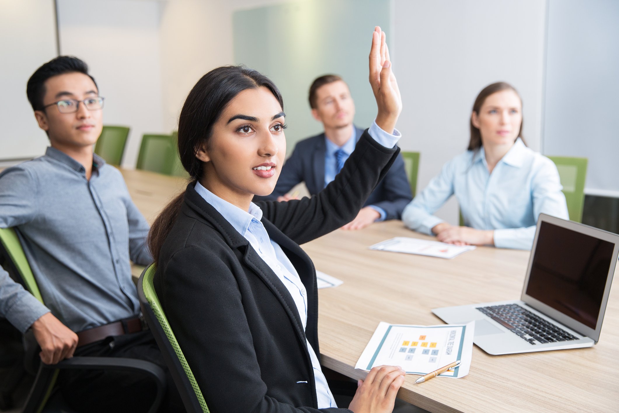 Professionally dressed woman raising her hand during a meeting