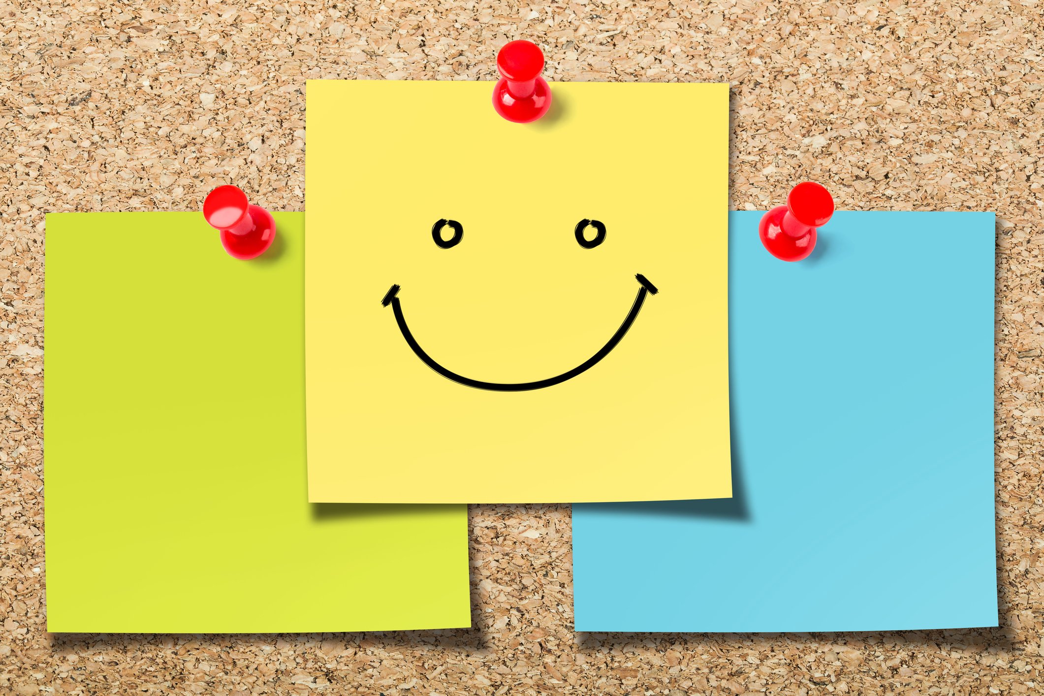 A cork board with smiley post-it notes.