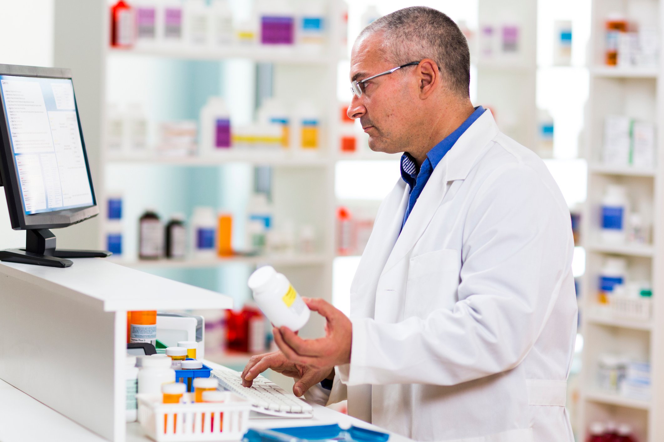 Pharmacist holding pill bottle and typing on computer keyboard