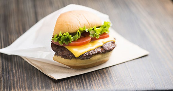 Shake Shack cheeseburger with tomato and lettuce tucked into a waxed paper bag, sitting on a napkin