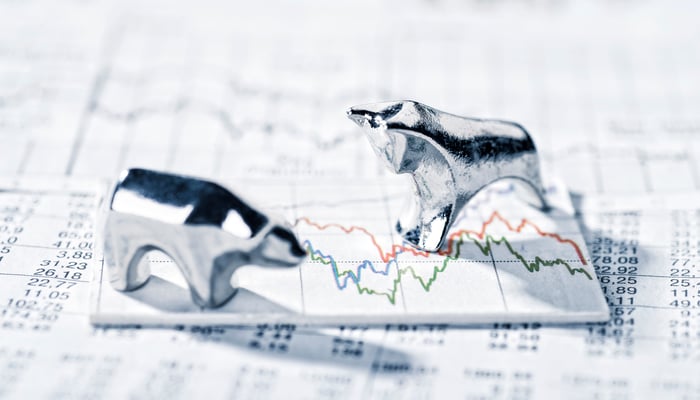 Pewter bull and bear standing on a stock chart over a sheaf of papers covered in numbers.