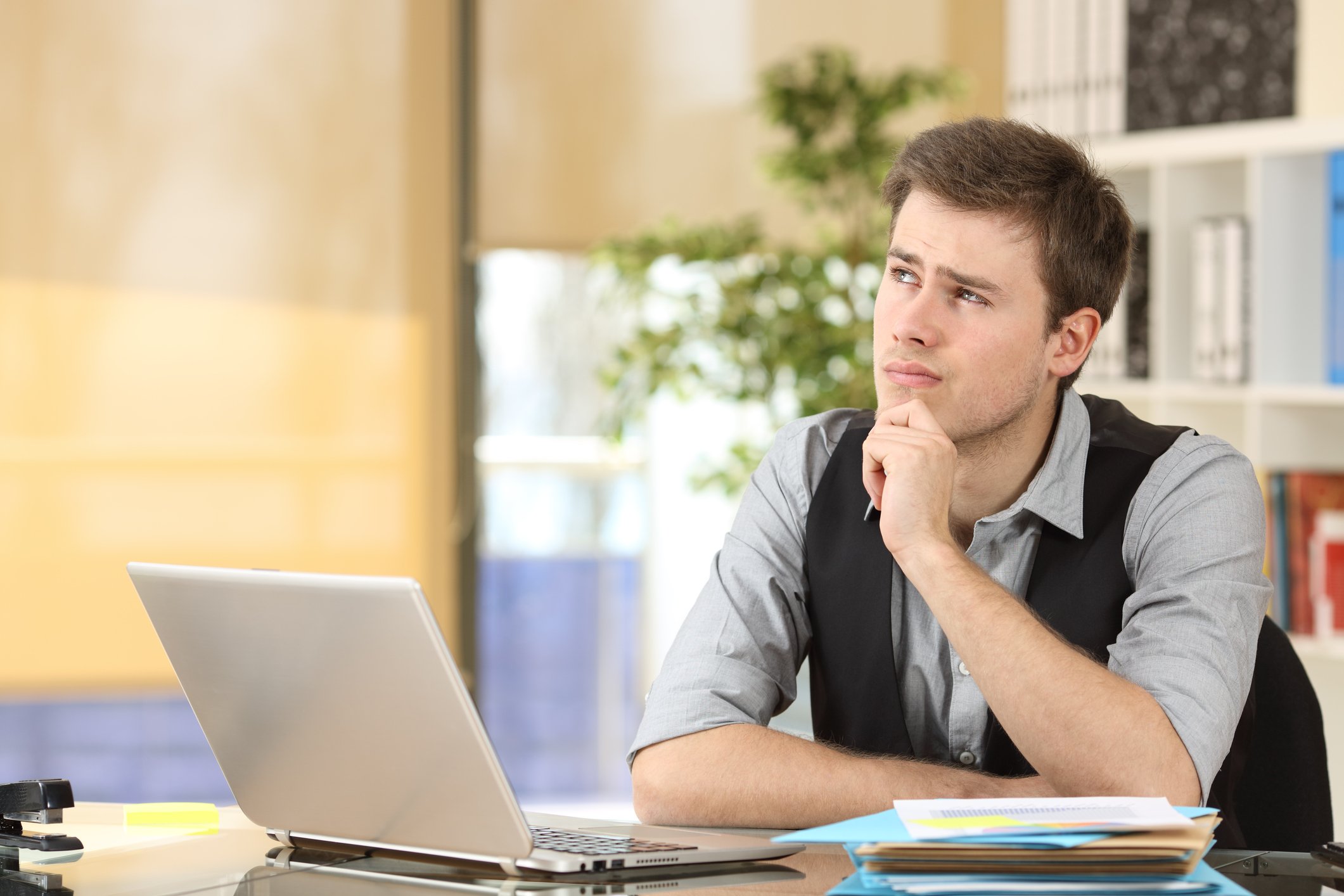 Man with laptop, pencil, and legal pads in deep thought at a desk.