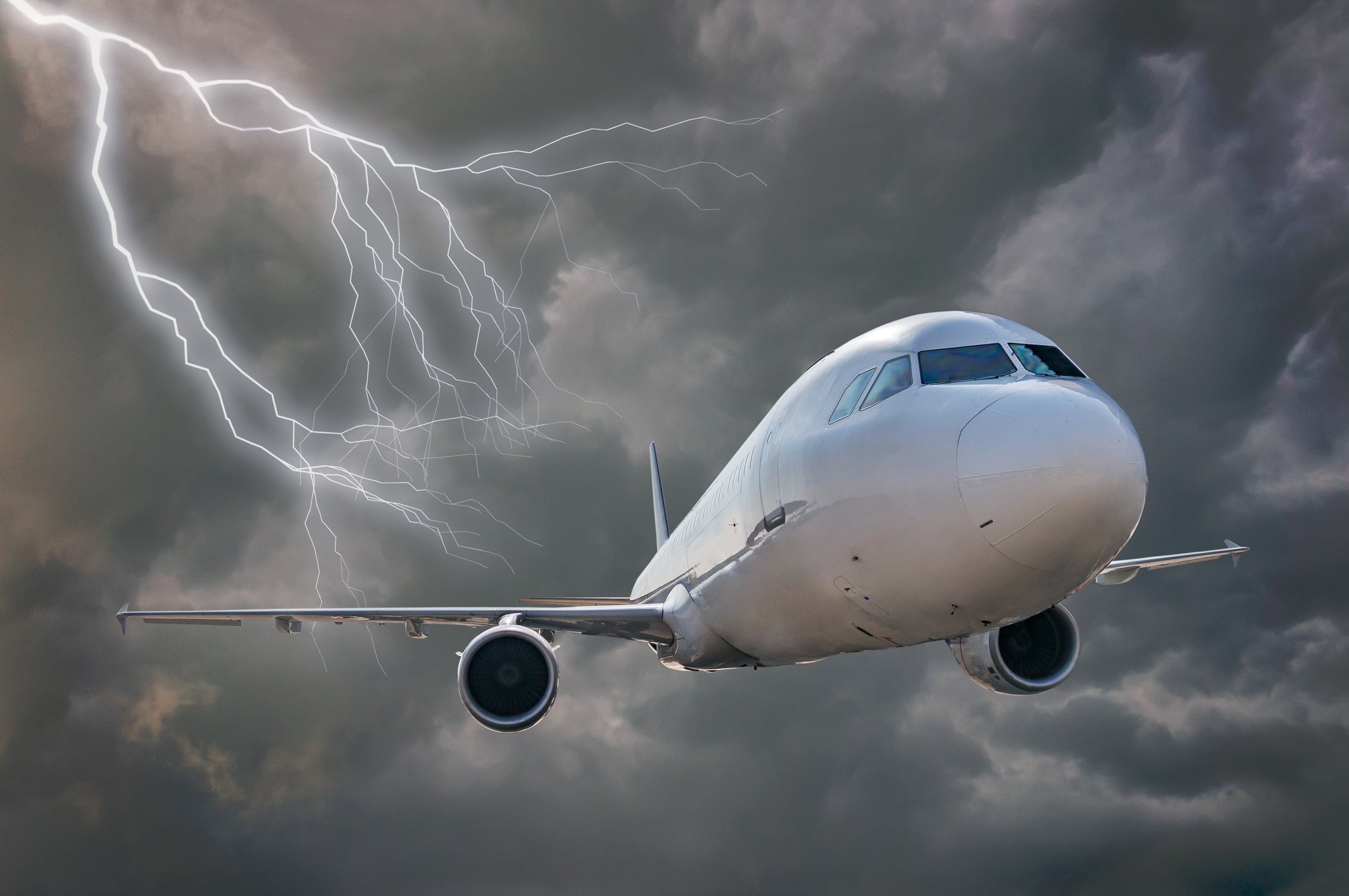 White passenger airplane flying through dark storm clouds and lightning strikes.