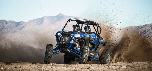 Polaris RZR Turbo kicking up dirt with two riders inside