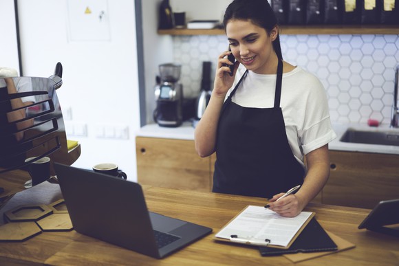 Woman in apron talking on the phone and writing on a pad