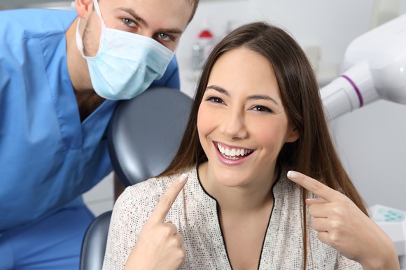 Dentist with young female patient pointing with both index fingers at her teeth