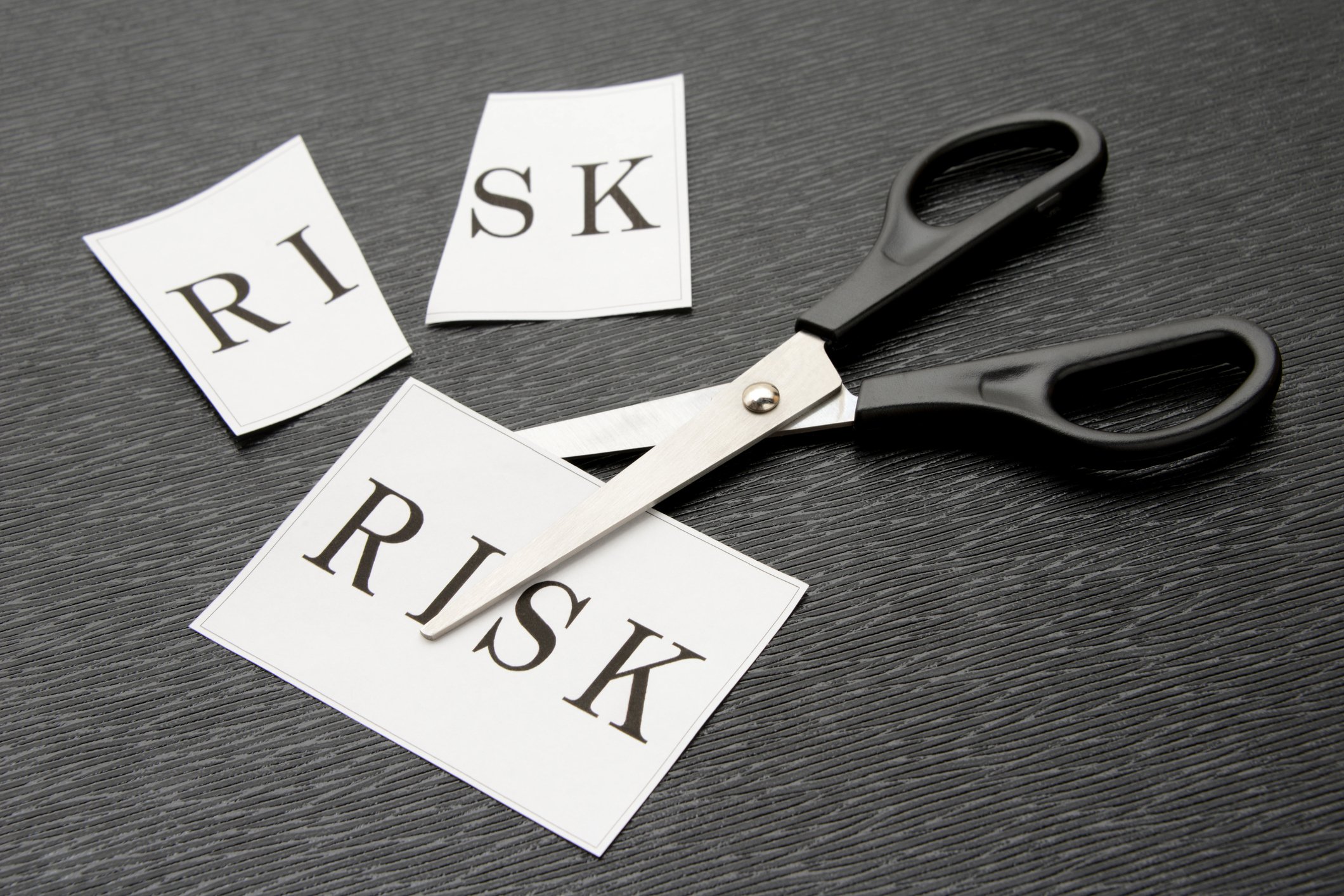 Paper with the word risk printed on it in between scissors blades next to an already cut piece of paper that had risk printed on it