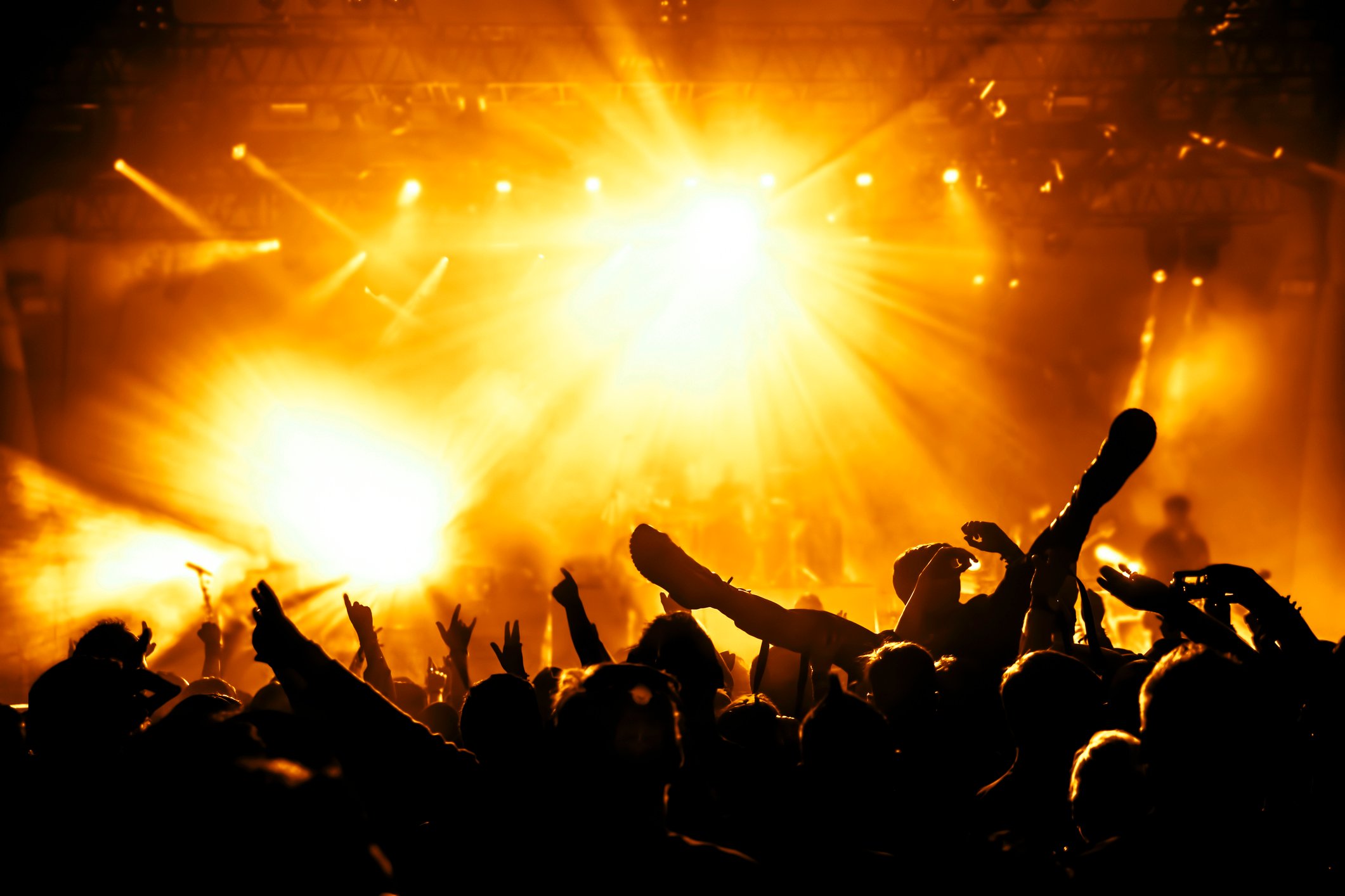 A rowdy crowd at a rock concert, bathed in yellow floodlights.
