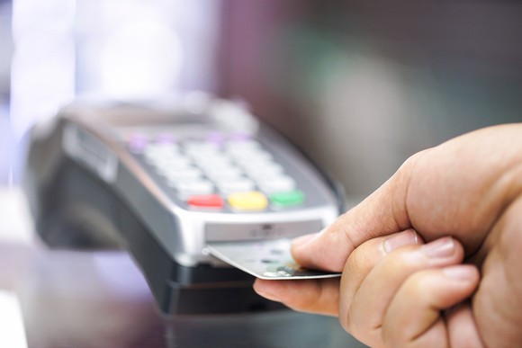 A hand inserting a credit card into a point of sale terminal.