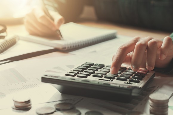 A woman typing on a calculator and recording numbers with her other hand