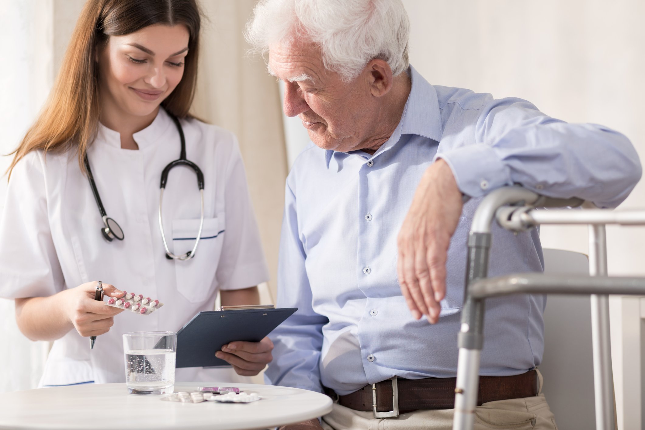 Person wearing medical scrubs and a stethoscope giving medication to senior male patient.