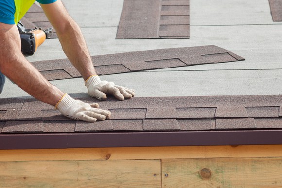 A worker installing asphalt shingles on a roof.
