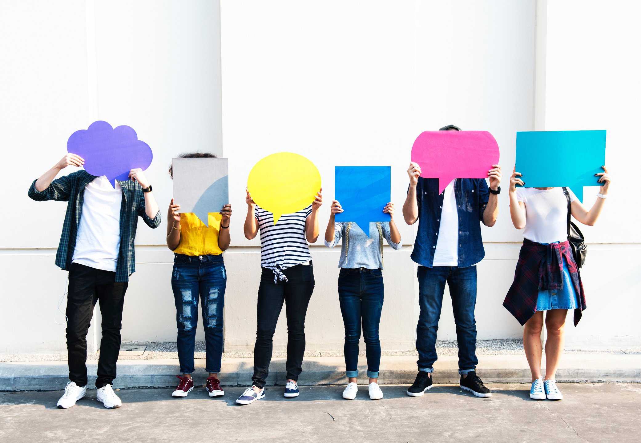 A group of apparently young people hold speech and thought bubbles in front of their faces.