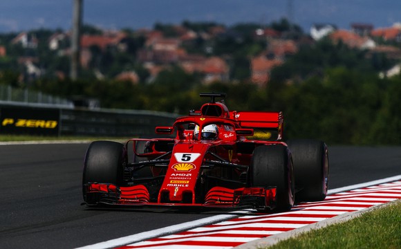 A red Ferrari Formula 1 race car wearing number 5 is shown at speed on a race track. 