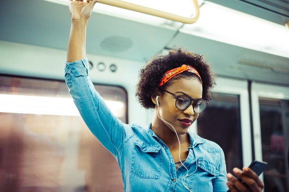 Young woman holding her smartphone listening to music on her daily commute