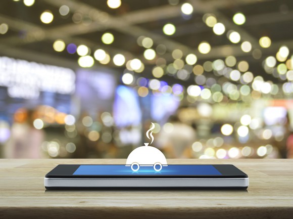 A food cart icon hovering above a smartphone.