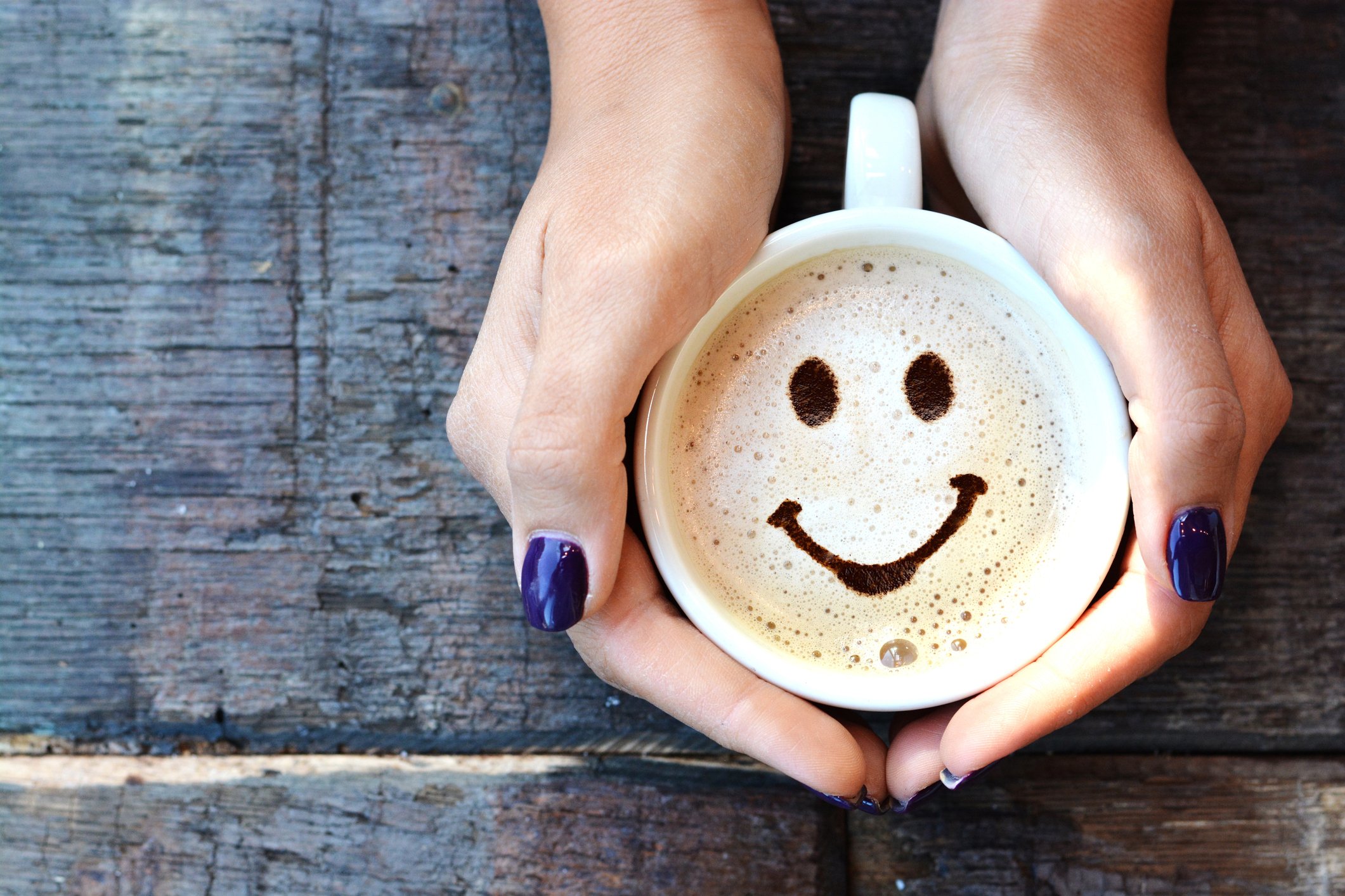A woman holds a cappuccino with a smiley face in the foam.