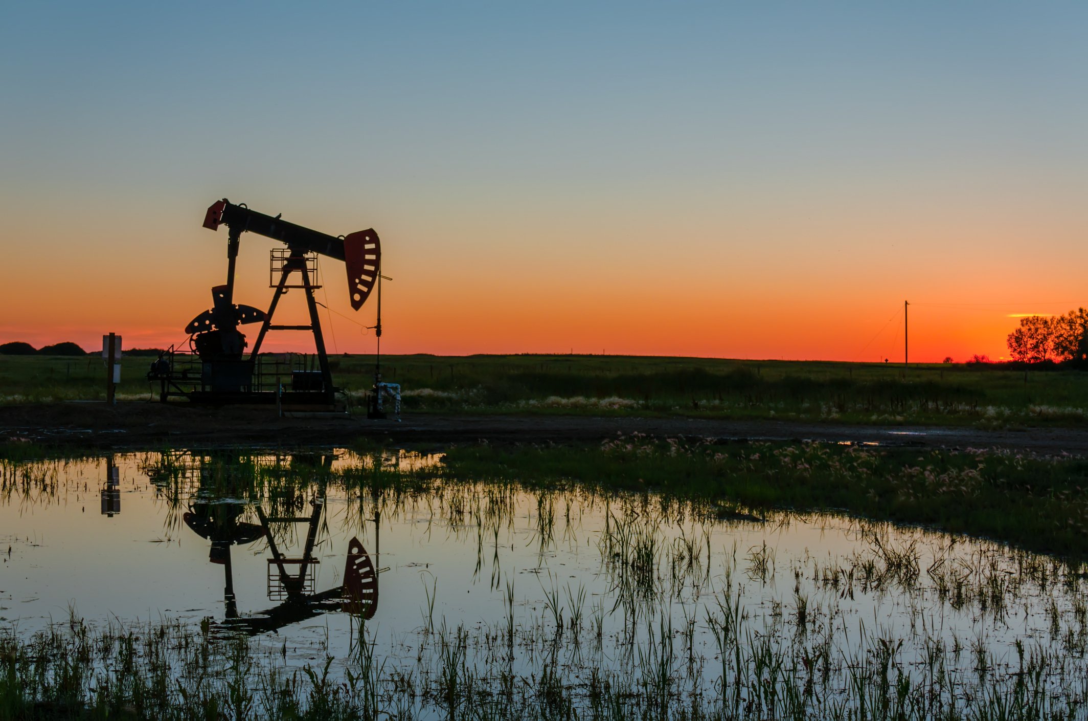 An oil pump next to a pond at sunset.