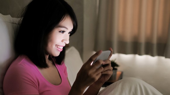 A woman on a couch is playing a smartphone game.