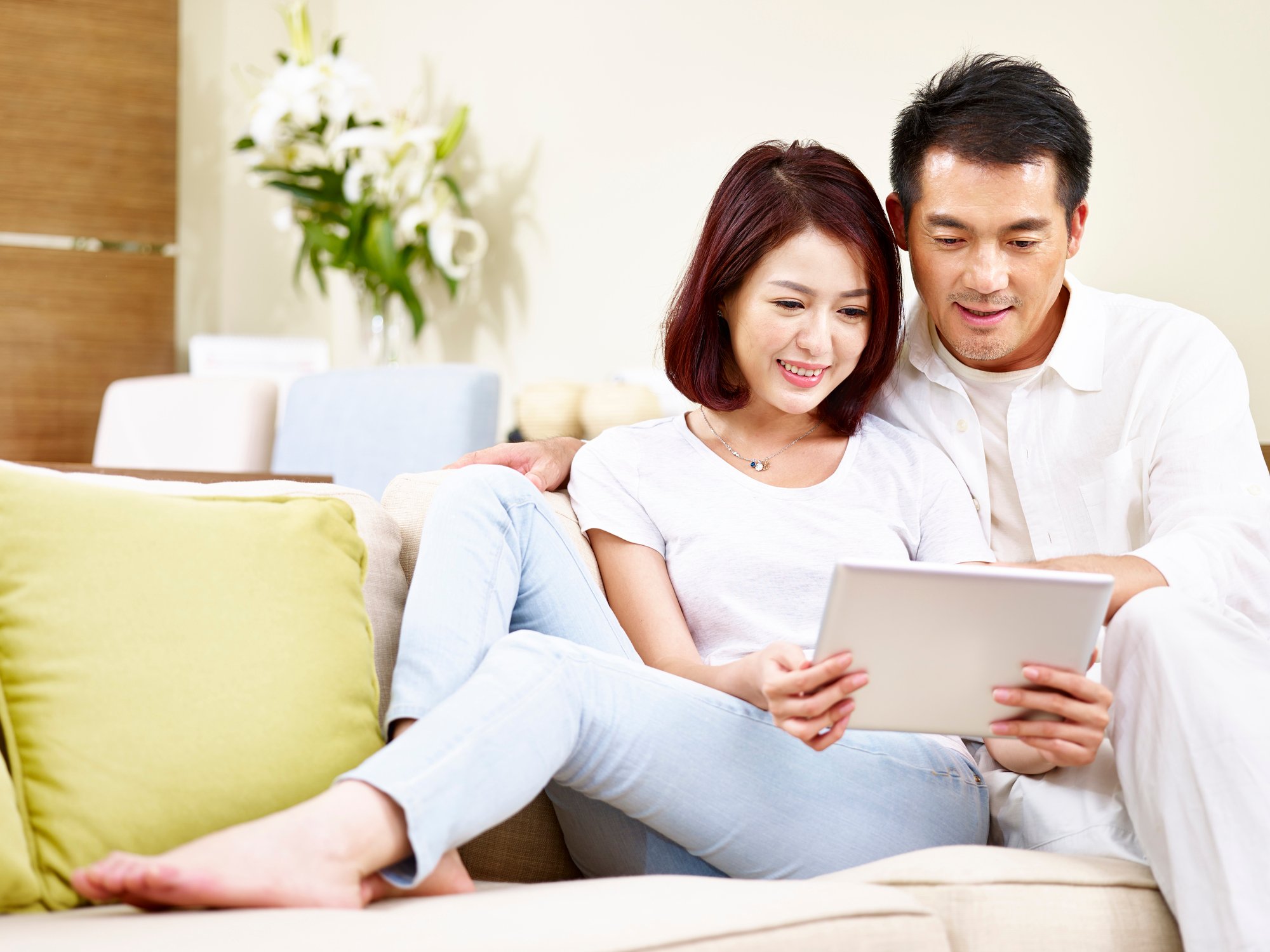Asian couple reclining on a couch and looking at a tablet