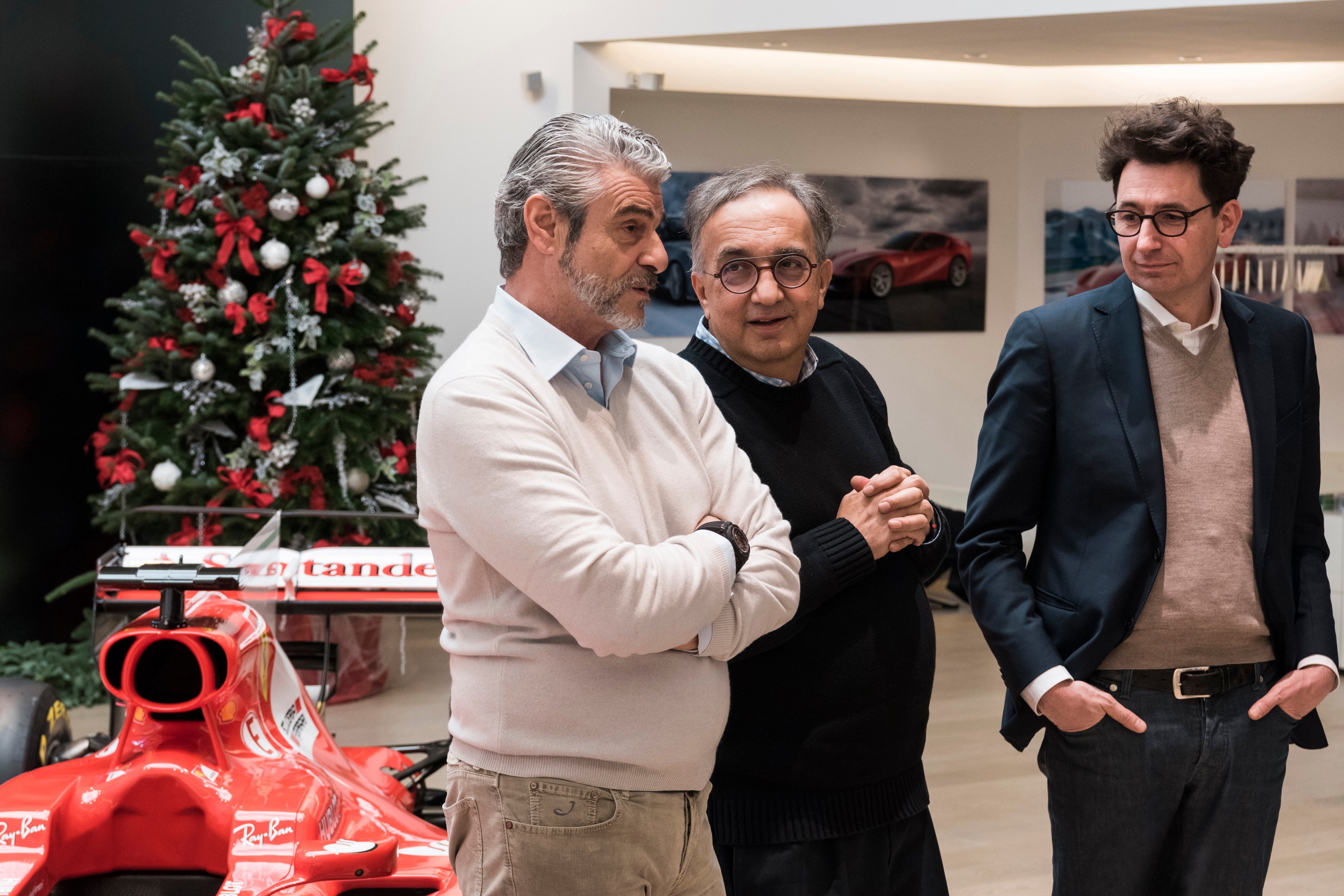 Marchionne is shown with two executives from Ferrari's racing team, at an event in December of 2017. A Ferrari Formula 1 race car and a Christmas tree are visible in the background.
