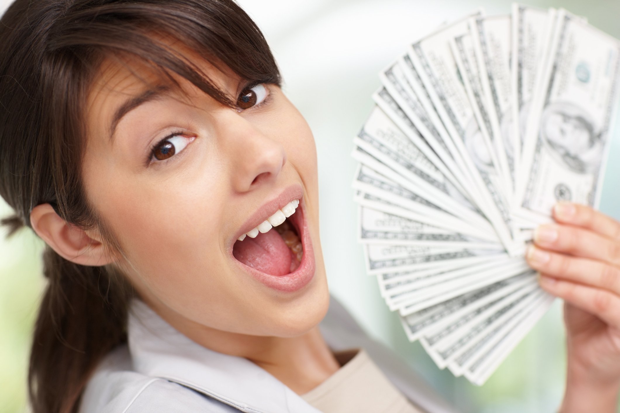 A surprised young woman holding a fanned pile of cash.