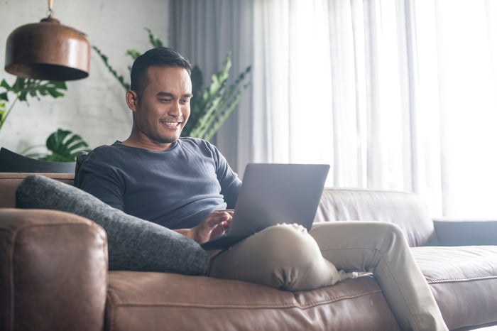 Man sitting on couch typing on laptop.