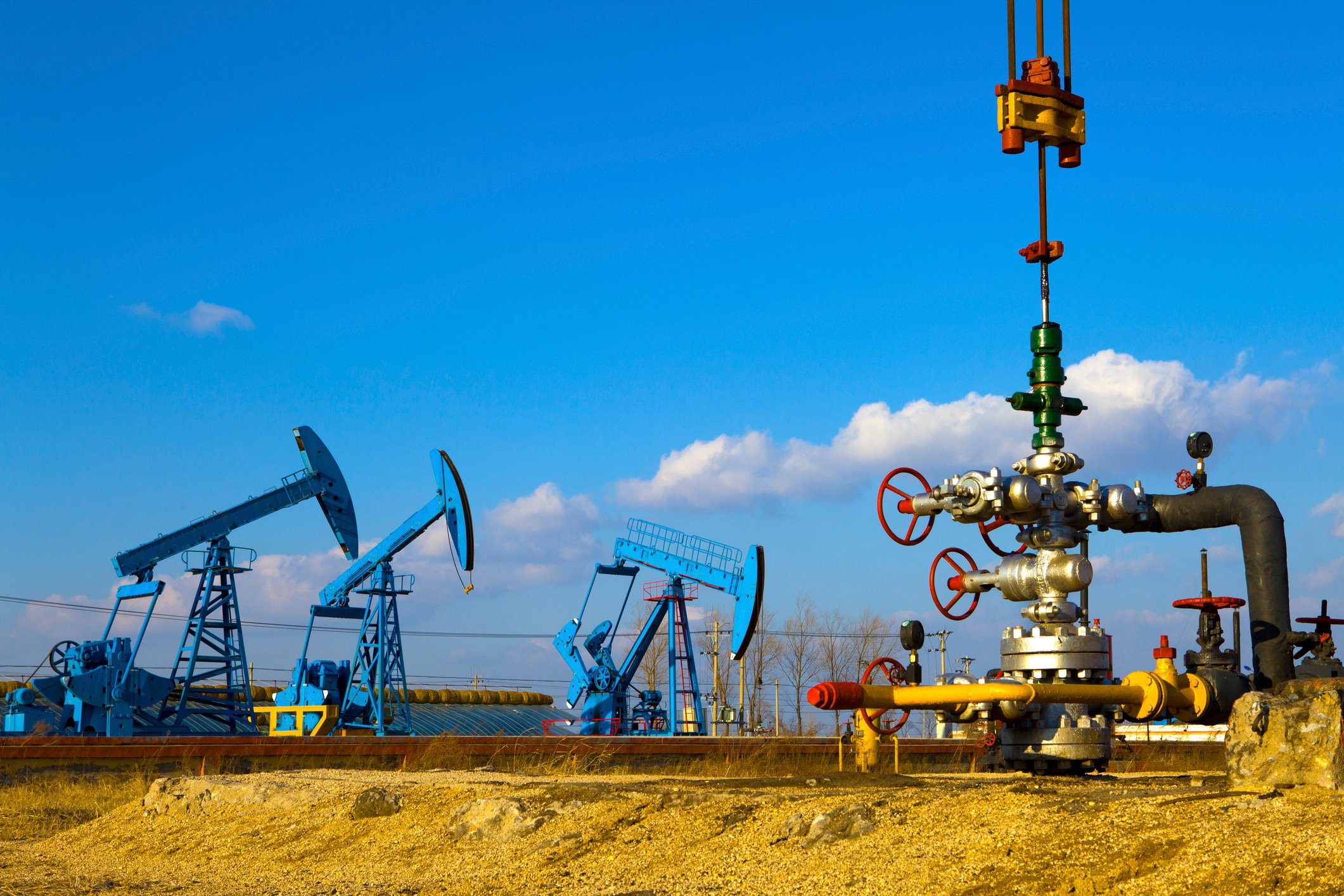 A close-up of a natural gas wellhead with three oil pumps in the background.