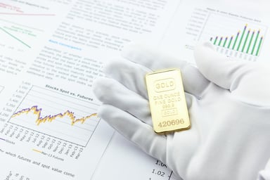 Gold Ingot Being Held With Stock Papers Getty