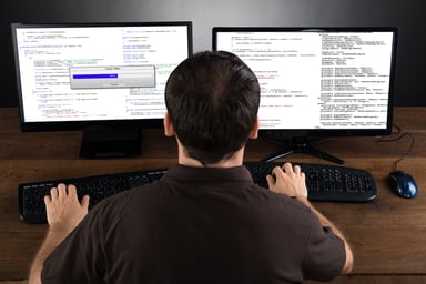 MAn sitting at computer with two monitors